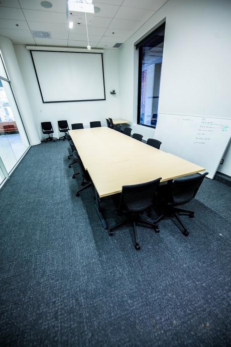 A long table with seats for up to 14 people with black chairs, a white board and large screen