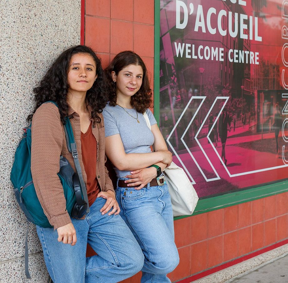 Concordia students leaning against the Welcome Centre wall