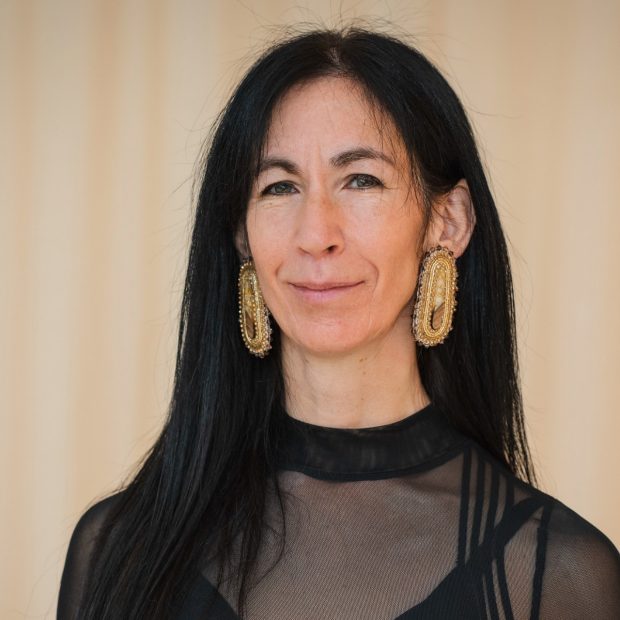 Barbara Kaneratonni Diabo Portrait of smiling woman with long, dark hair and funky, bold, gold earrings