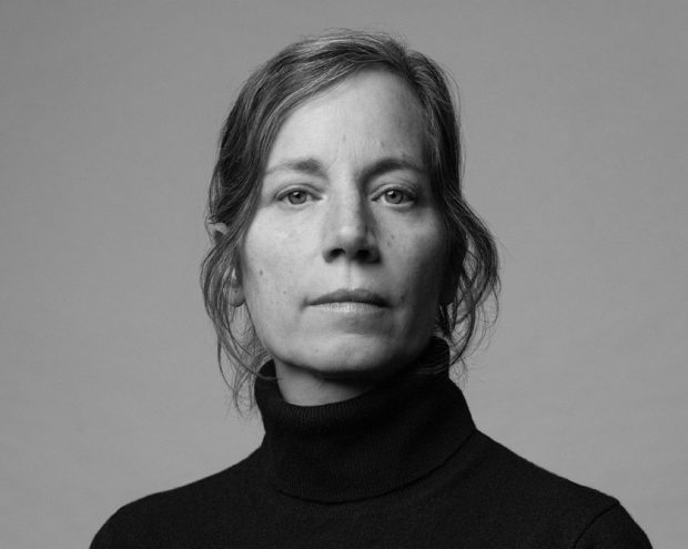 A woman with short black hair and wearing a black hoodie spreads her arms open.