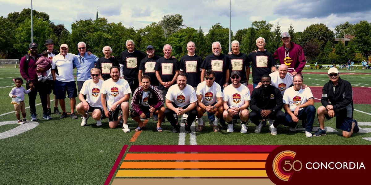 Alumni soccer players stond on the pitch and smile.