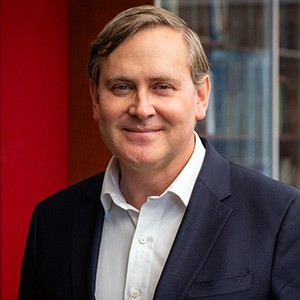 Patrick Shea wears a white shirt under a blue jacket. He has short light brown hair.