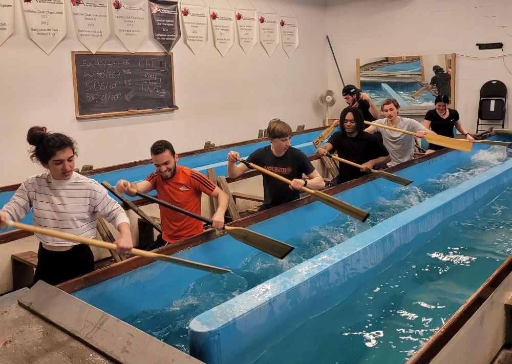 Seven Concrete Canoe team members practicing their paddling in an indoor environment.