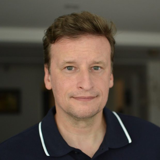 Headshot of a man with brown hair wearing a navy blue polo shirt with a white stripe around the collar.