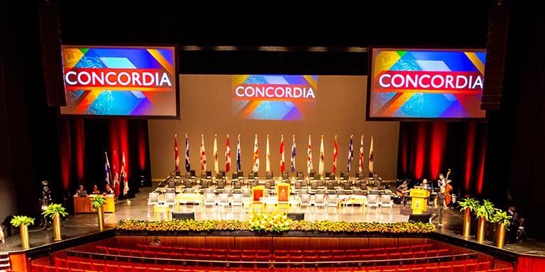 The stage at Place-des-Arts is ready for Spring convocation with, flowers, flags, chairs and screens