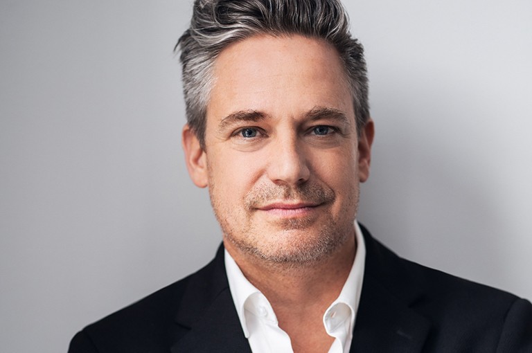 A man with salt and pepper grey hair stands against a white background