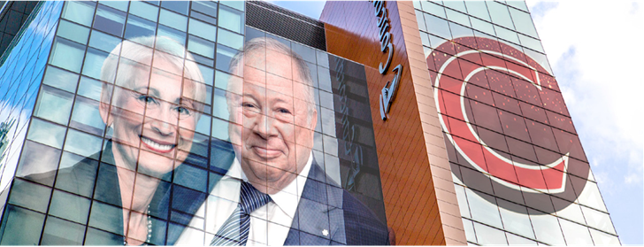 A modern Concordia University building with large glass windows. Superimposed on the windows are portraits of an older man and woman, both smiling and dressed in formal attire. The Concordia logo, a large stylized "C", is prominently displayed on the right side of the building. 