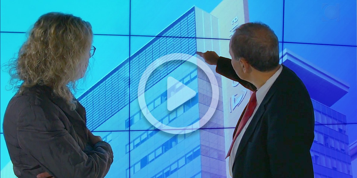 Two individual stand looking at a screen pointing to a building