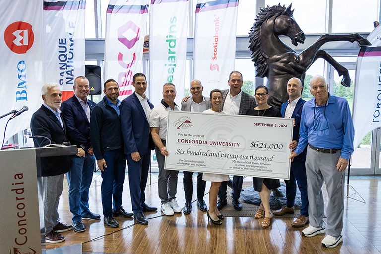 Eleven people stand in a line and hold a large cheque in the amount of $605,000