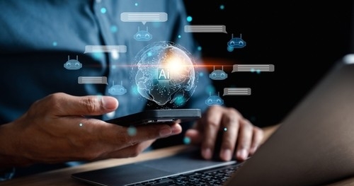 A man at a laptop holds a mobile phone
