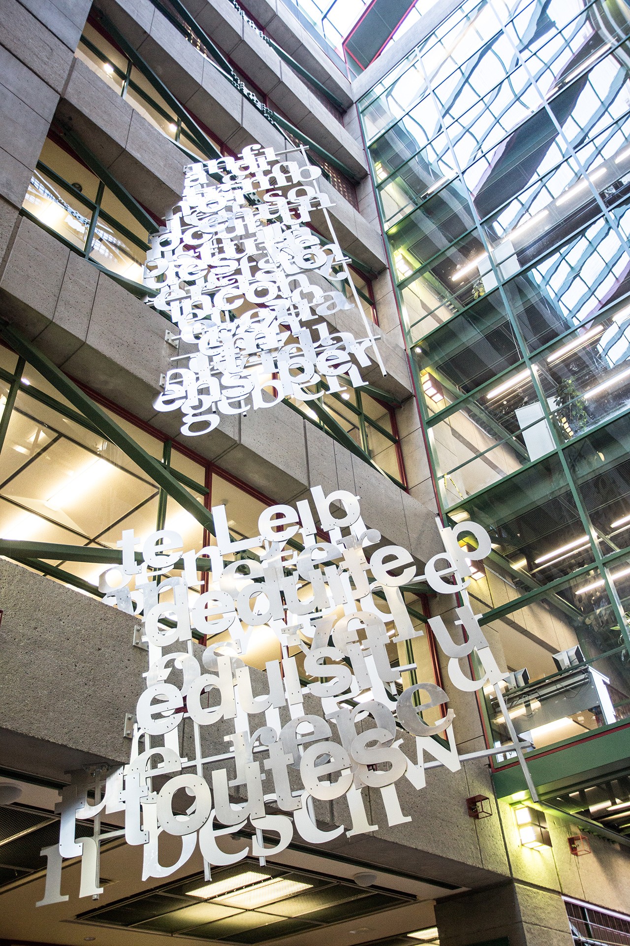 Untitled by Rose-Marie Goulet with Effets Publics A pair of grids on which metal letter forms and word fragments are suspended from the ceiling. The height of the two grids is at least two and a half storeys.
