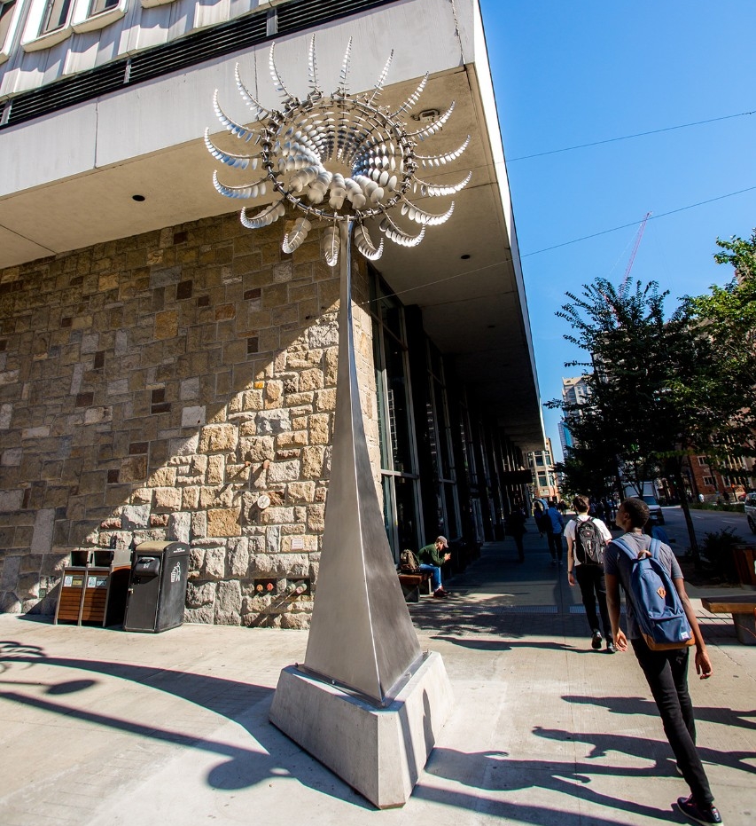 Di Octo II by Anthony Howe A stainless-steel sunflower, over seven meters tall standing outside on a sunny corner. Each petal on the sunflower is built from circles that gradually increase in size from tip to mid-point, then decrease in size to the end tip at the centre of the flower. The petals catch the wind so the sunflower appears to be blooming.