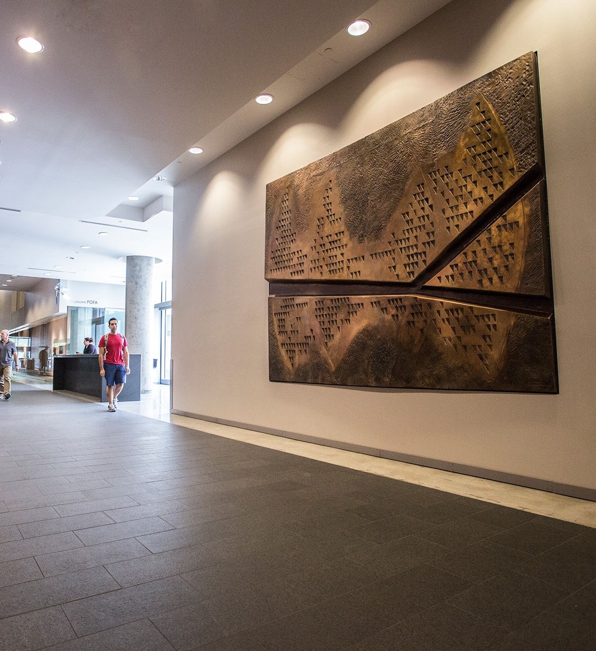 Trans-Earth by Yves Trudeau A wall-mounted bronze panel sculpted in a bas-relief style. The piece resembles a map of a biblical land, featuring dozens of triangles cut out from the surface. A deep canal bisects the work, beginning on the left side, and opening to a Y shape on the right, suggesting three separate sections to the work