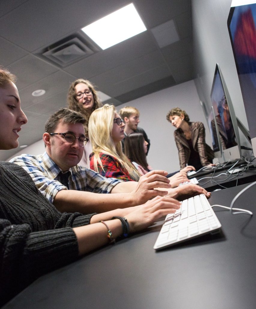 A professor discusses with students in a computer room in a classroom setting