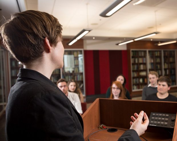 A women holds a book, while a library setting sits slightly out of focus in the background