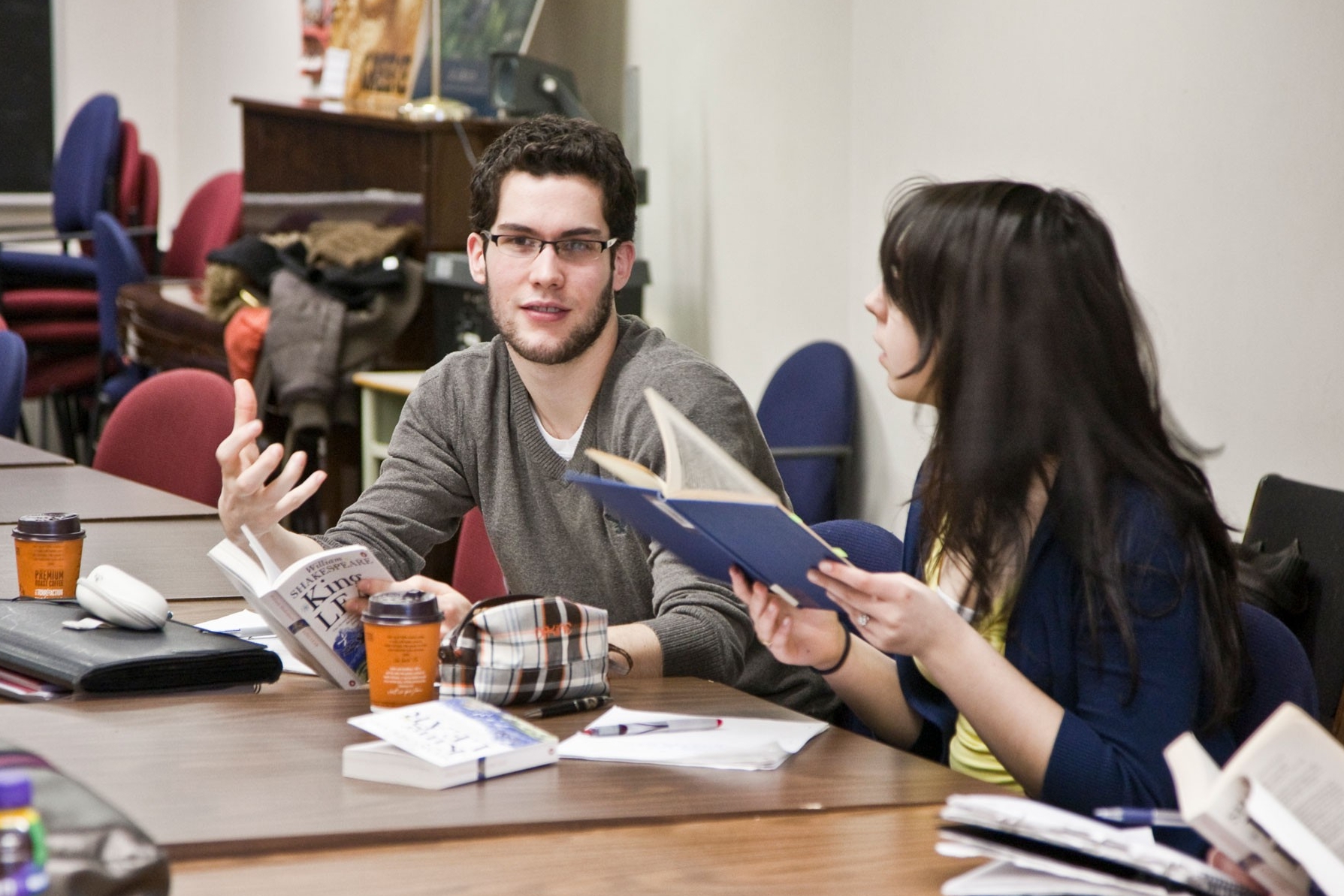 Two Liberal Arts College students hold books and discuss the readings in class.