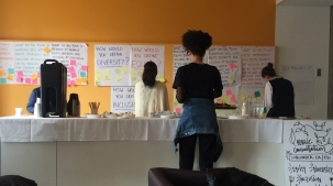 A photo of three people standing with their backs to the camera adding text about equity, diversity, and inclusion to white posters taped to an orange wall