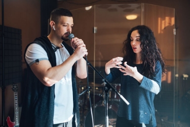 Speaking exercise with a woman coaching a young male wearing earphones speaking into a microphone