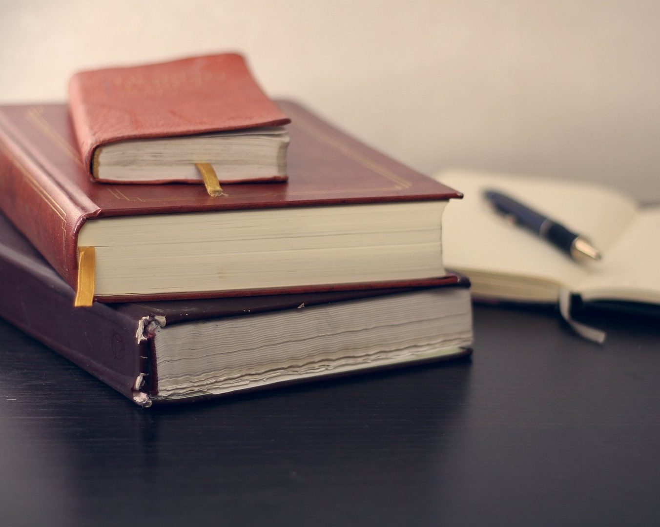 Une pile de livres et un stylo reposant au milieu d’un carnet ouvert.