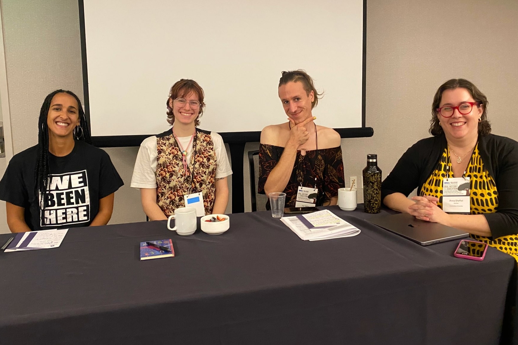 4 smiling people seated at a long table at the front of a room