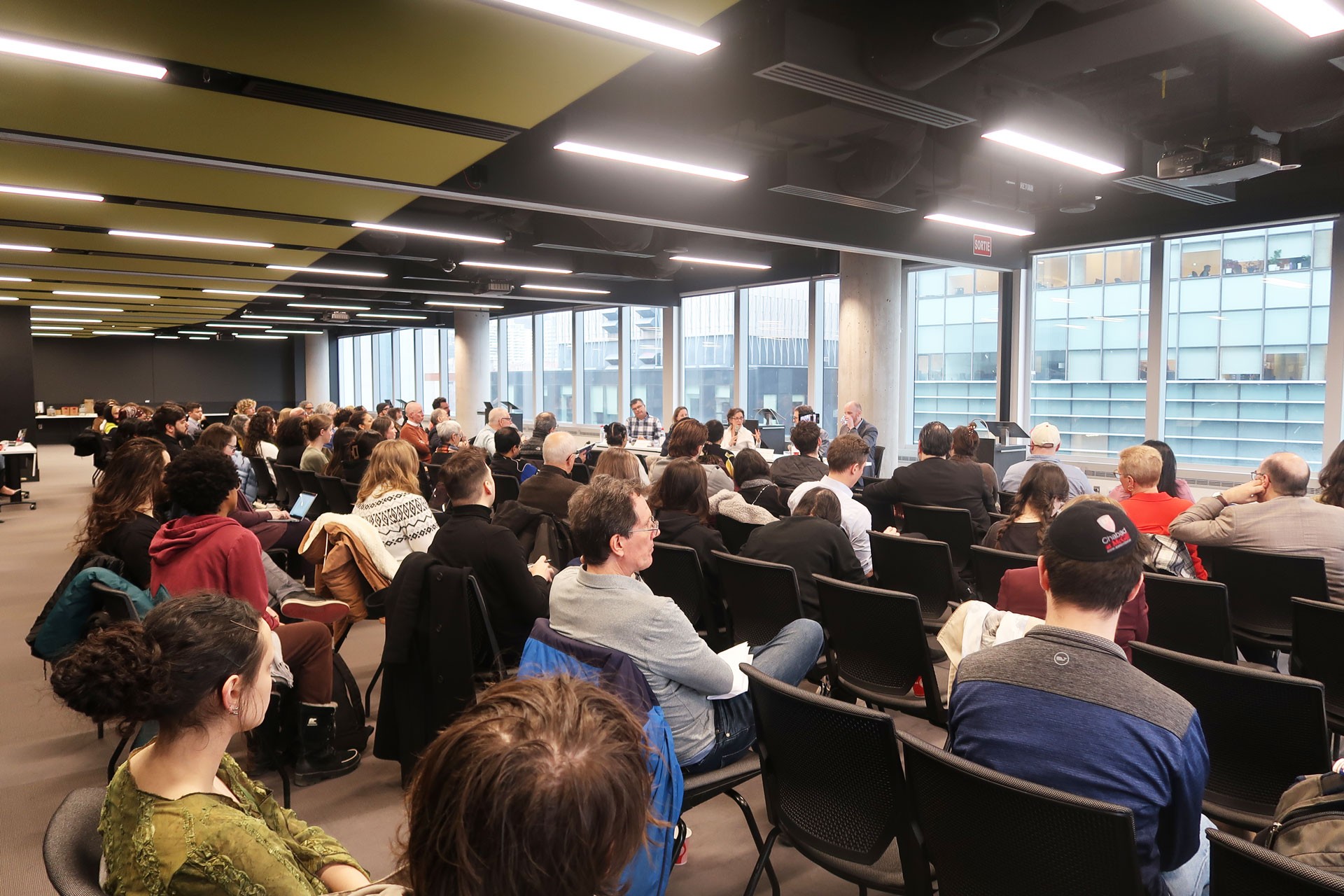 an audience faces a panel of 5 speakers at a table