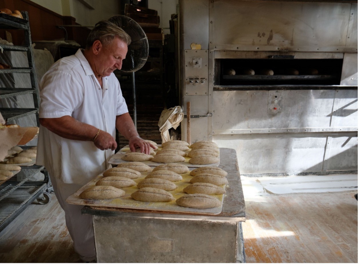 A baker prepares loaves of bread for the oven
