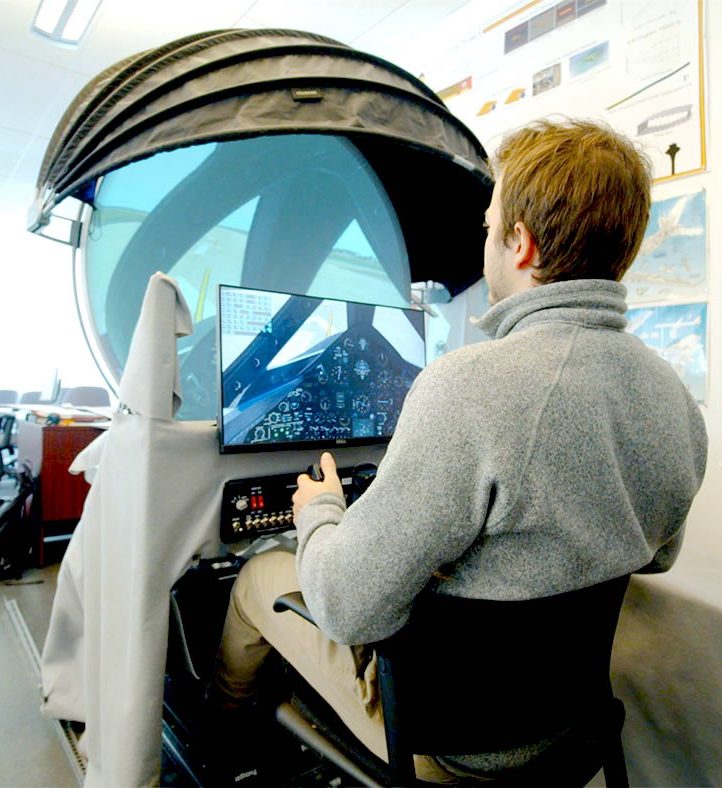 A man sits in front of a flight simulator in an aerospace training lab