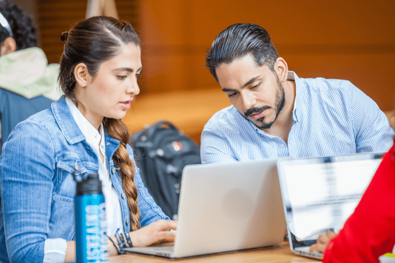 A woman and man seated and looking at a laptop screen together. A woman and man seated and looking at a laptop screen together.