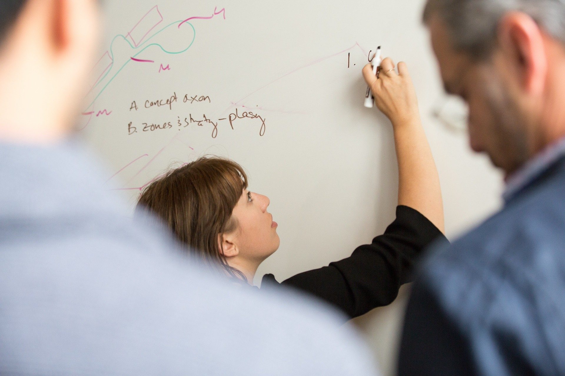 A female writing content on a whiteboard using a black whiteboard marker. 