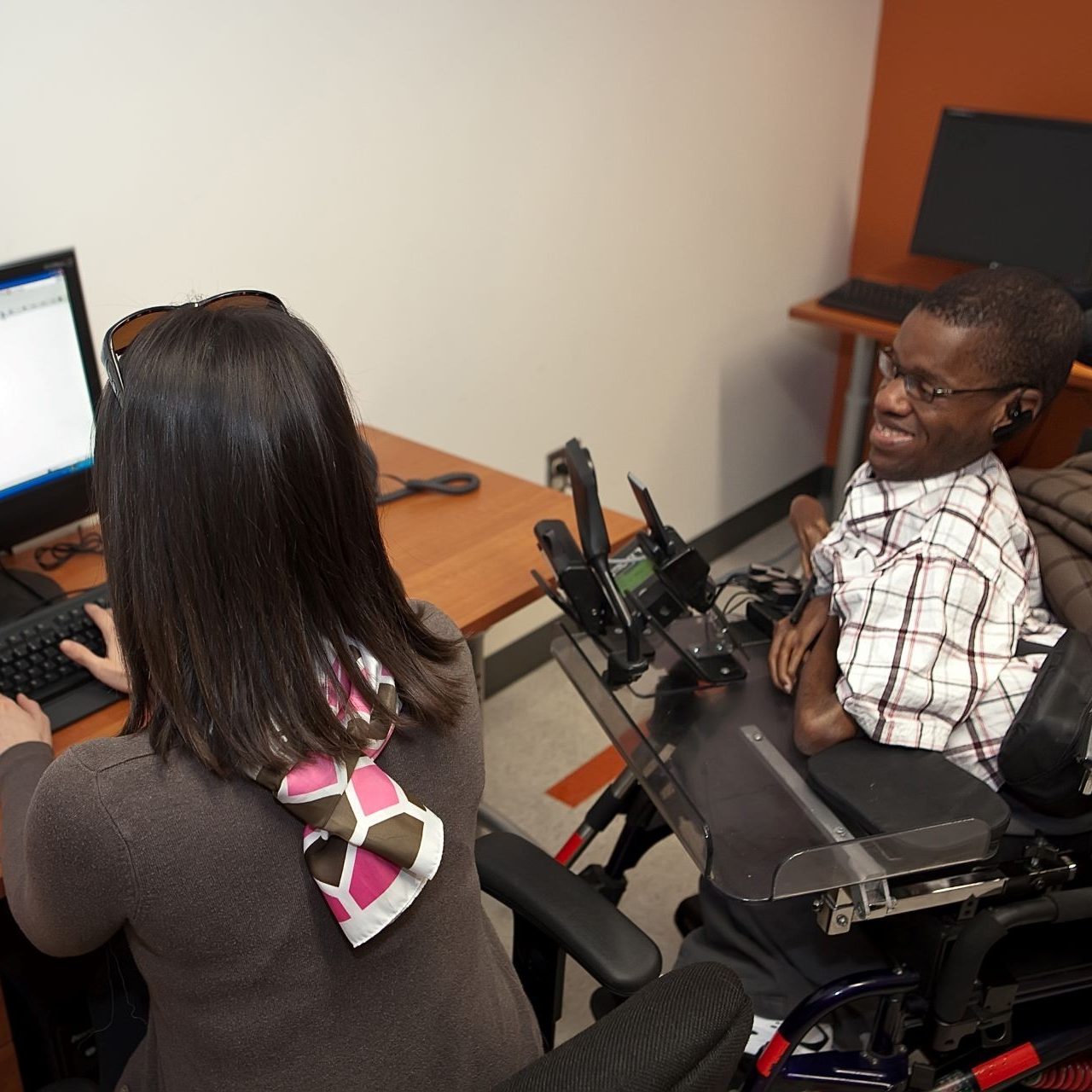 Woman in wheelchair waving hello in front of a laptop and wearing earbuds