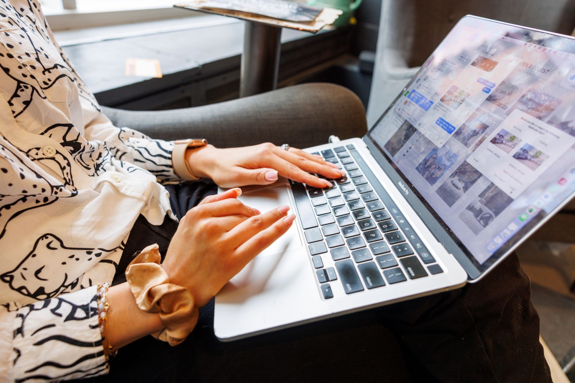 Photo of person seated on a chair typing on a computer laptop. The laptop is resting on their lap the photo does not show the persons face but is focused on hands typing on the laptop.