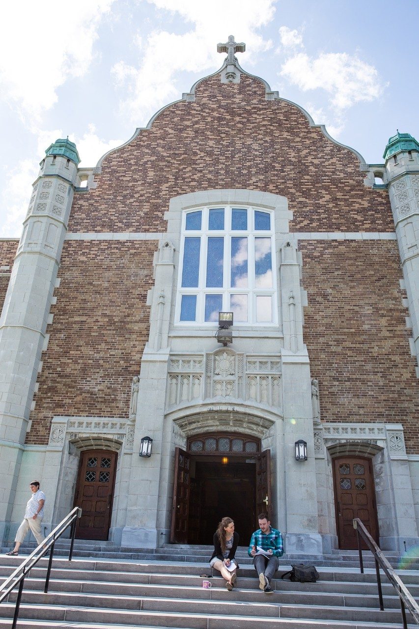 Two students sit on the steps of the Loyola Chapel at Concordia