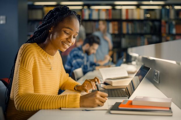 Black student writing with laptop and books