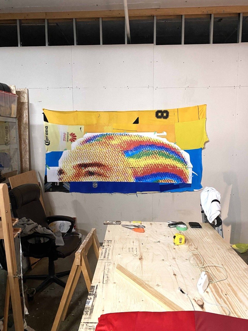 Studio shot, the artwork is visible in the background, patchwork of colorful sports jersey with a low quality impression of the reggaeton singer J Balvin, wearing multicolor cornrows