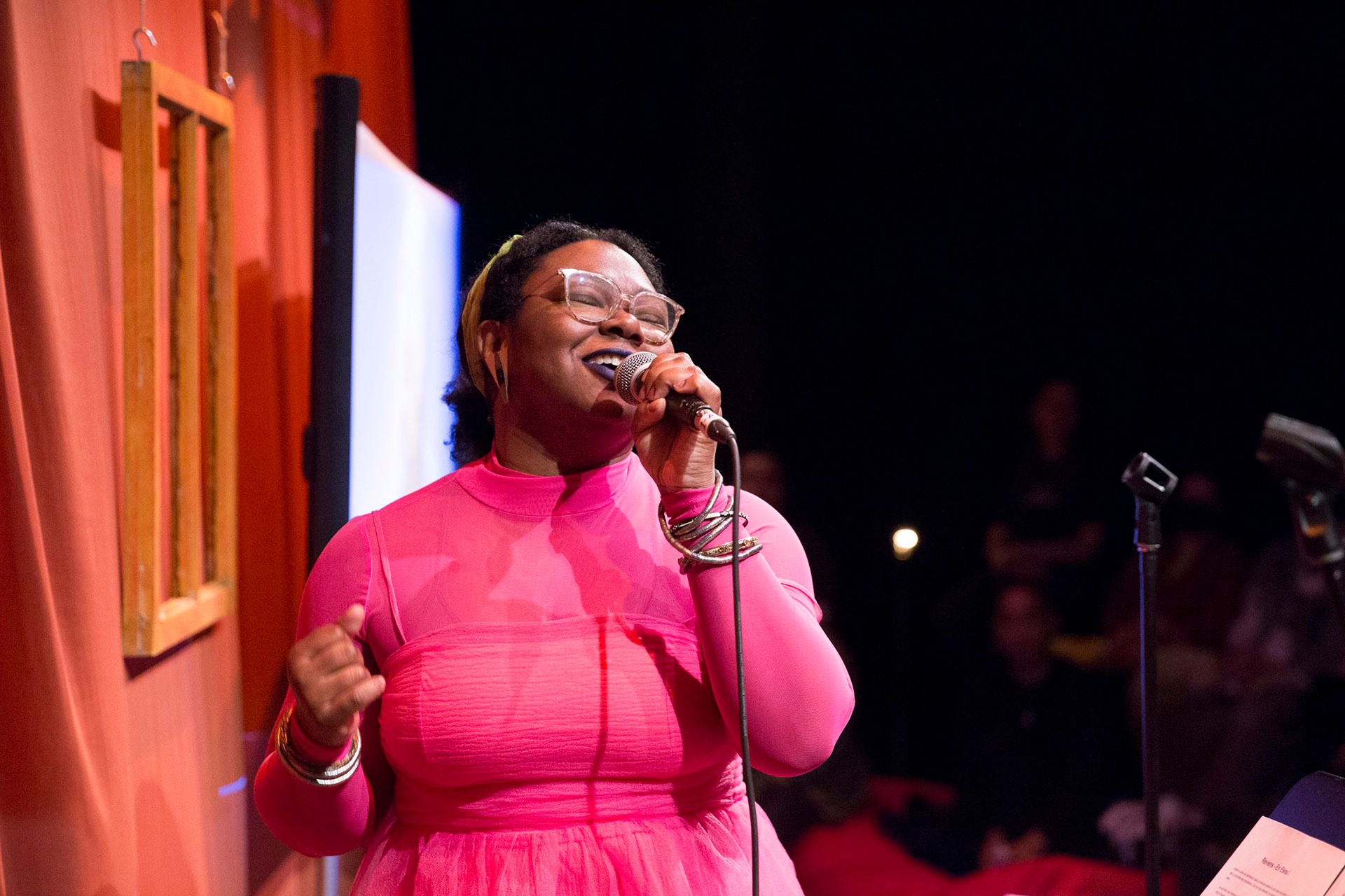 Two female presenting sisters who identify as Black are sitting in the washroom, the youngest is braiding the oldest hair. 