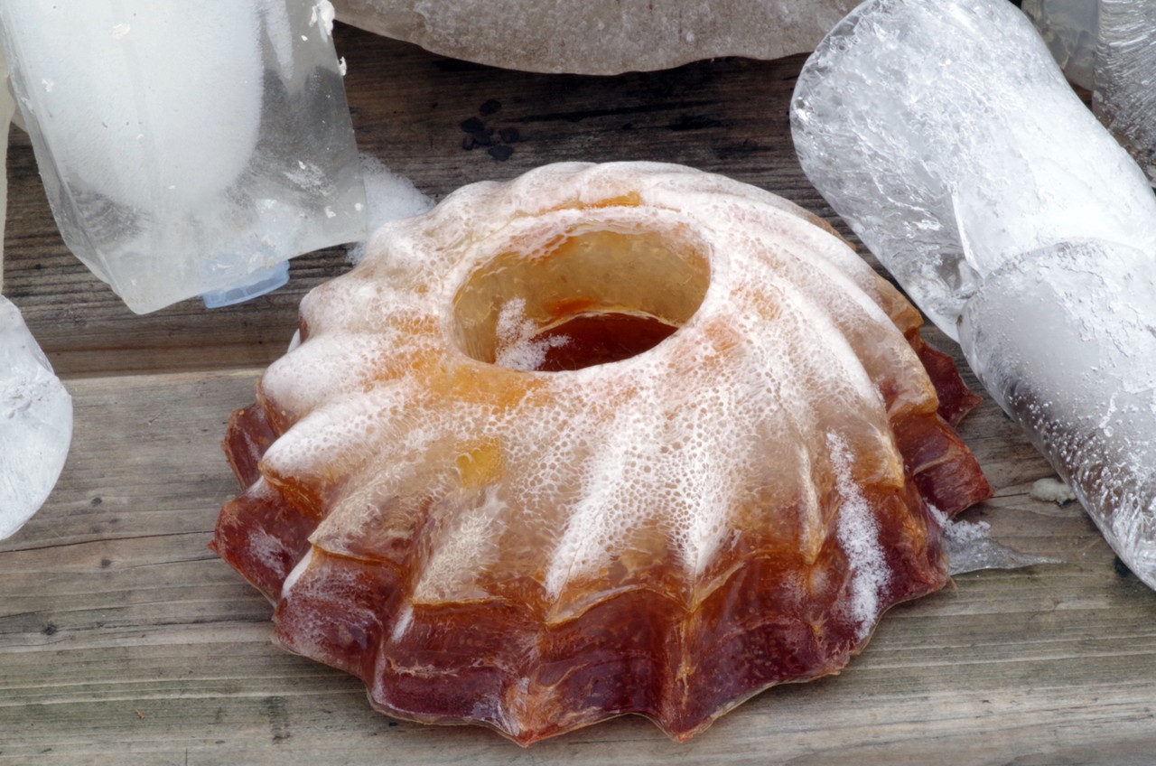 Photographie détaillée d'un récipient en plastique contenant un dessert et de l'agar congelé, teinté d'orange foncé à clair.