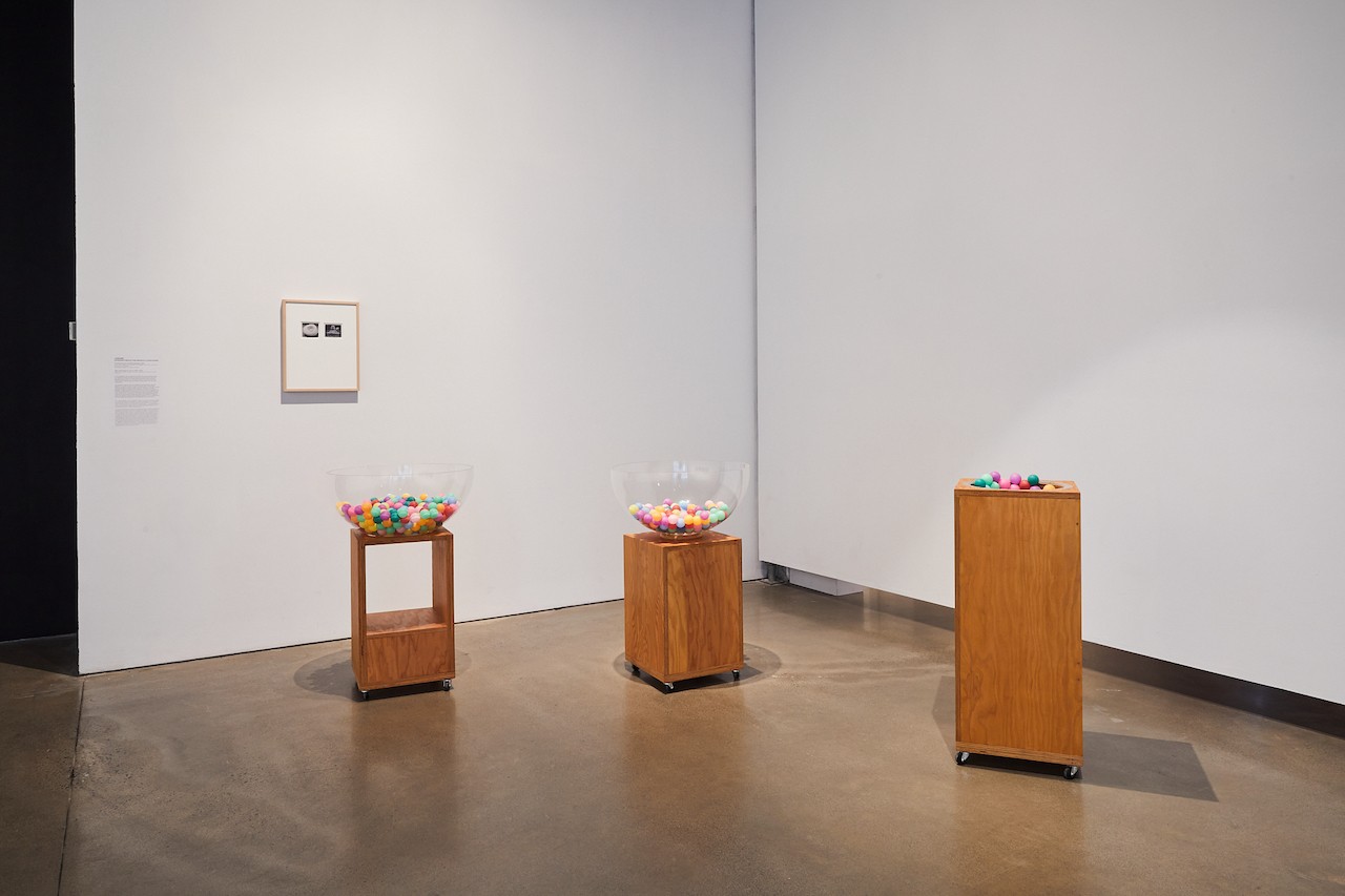 An art gallery installation of three differently designed plinths holding mutlicolored ping pong balls. The artworks are within a white walled gallery.