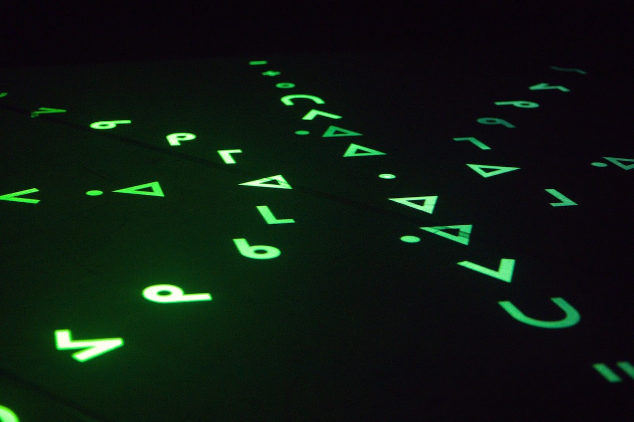 a black floor with bright green letters and symbols projected on it in a radiating shape. 