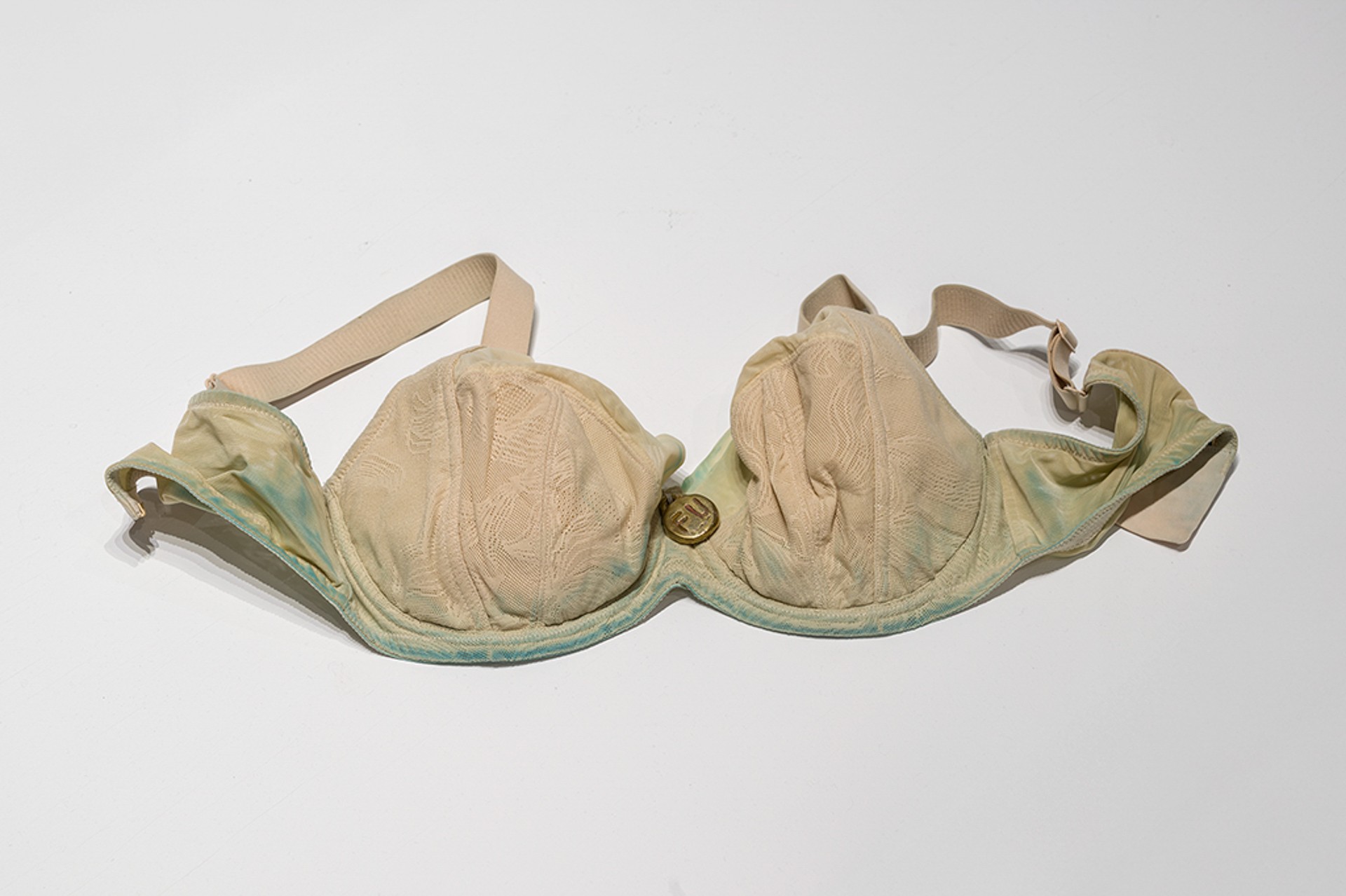 close photograph of an old beige bra that has greenish stains along the seams.