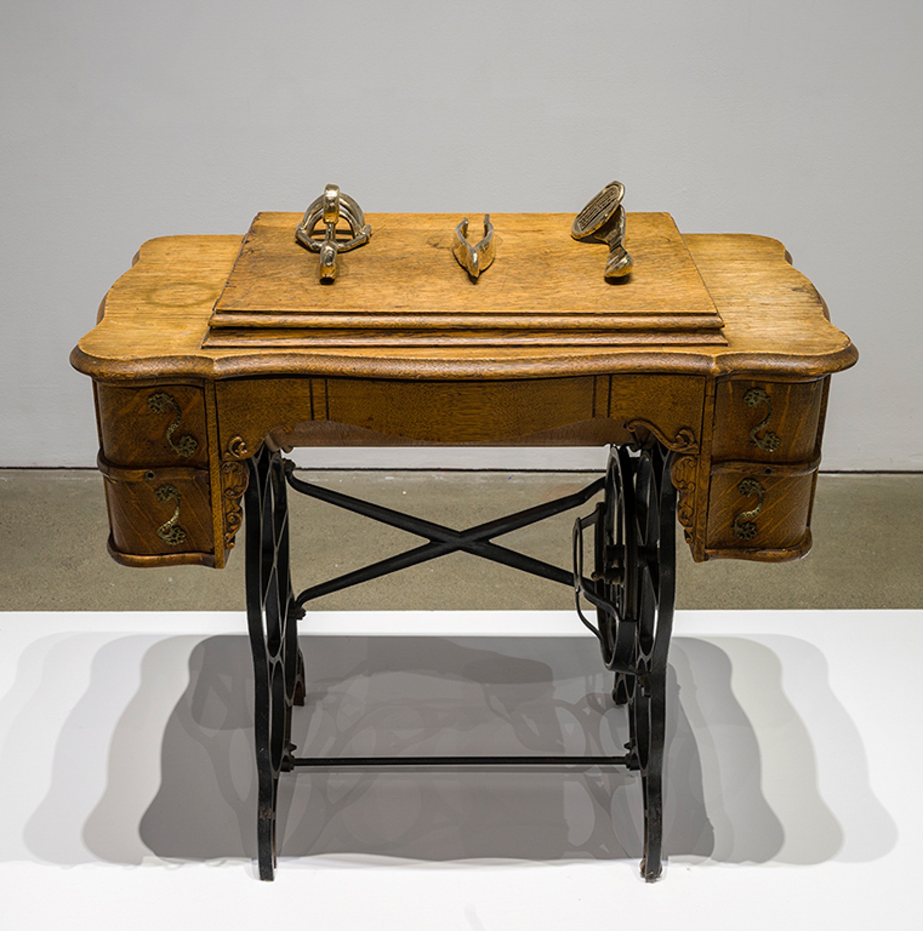 Ornate sewing table with three bronze objects laid on its surface: oversized lash curler, tweezers, and disposable razor