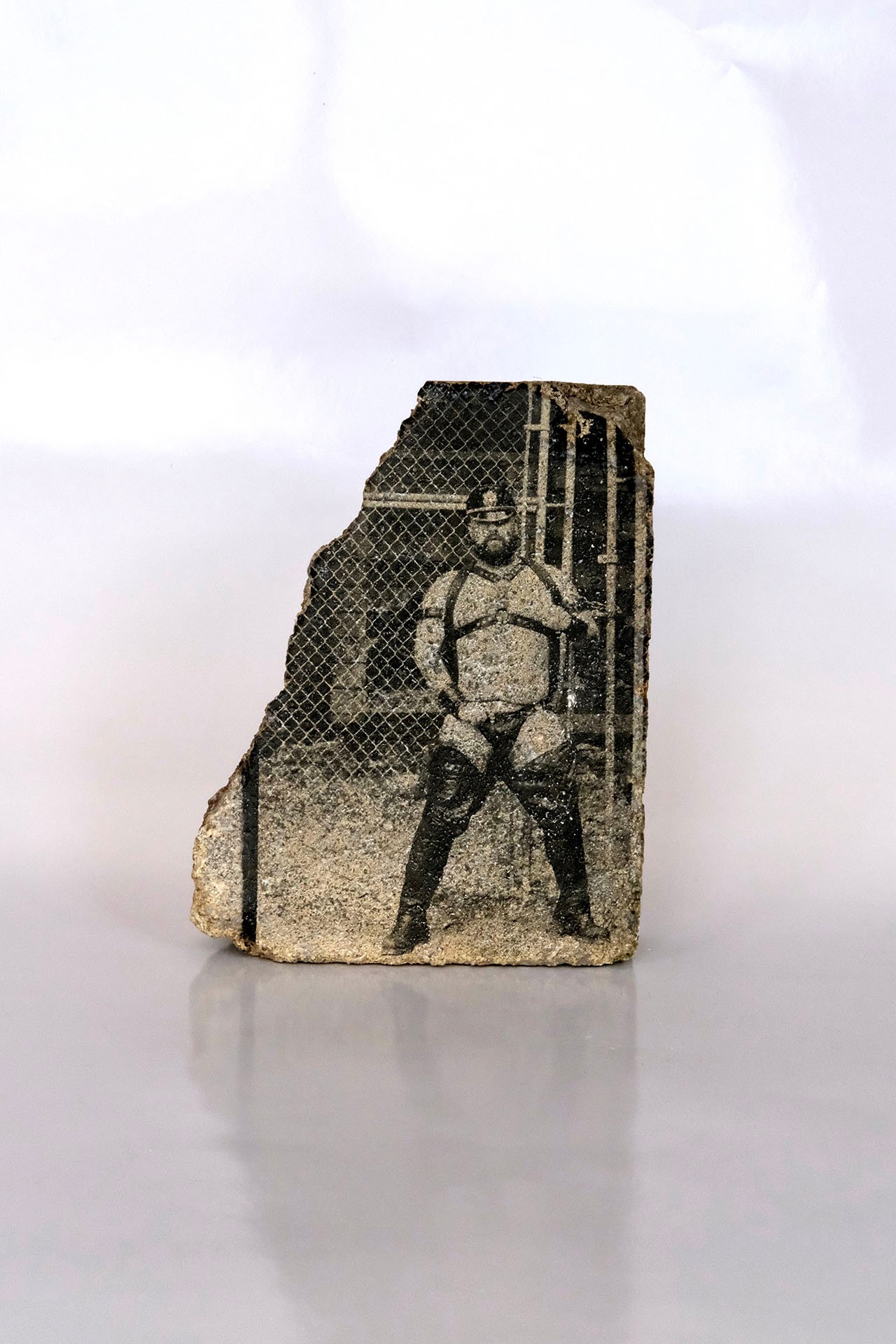 Image d'un homme vêtu de cuir, photographié accoté sur une clôture. Cette image a été transférée sur une roche plate.