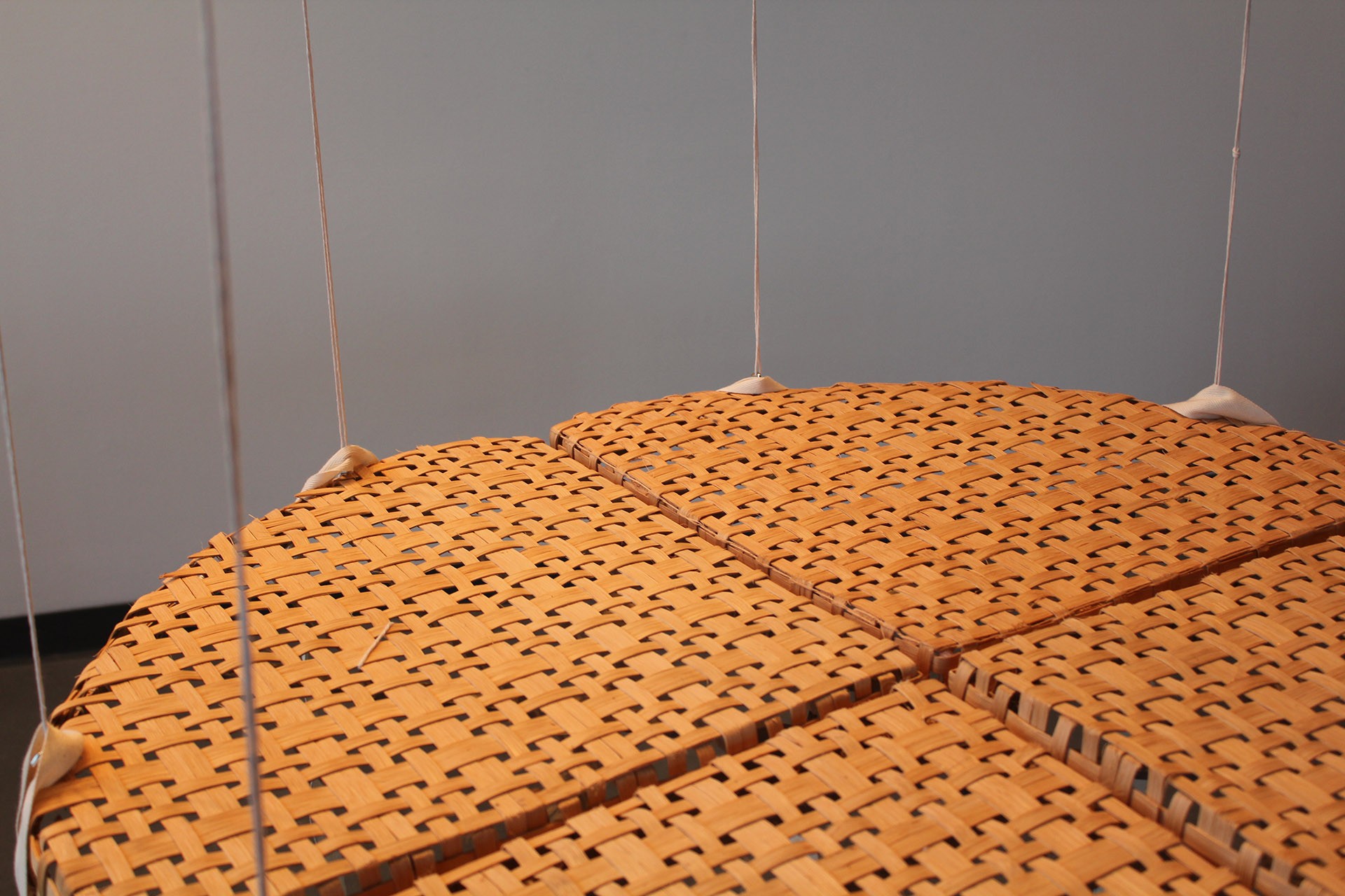 L'œuvre d'art est une table ronde faite de roseau plat brun clair et suspendue au plafond. La table est divisée en quatre et cette photographie en capture la plupart.