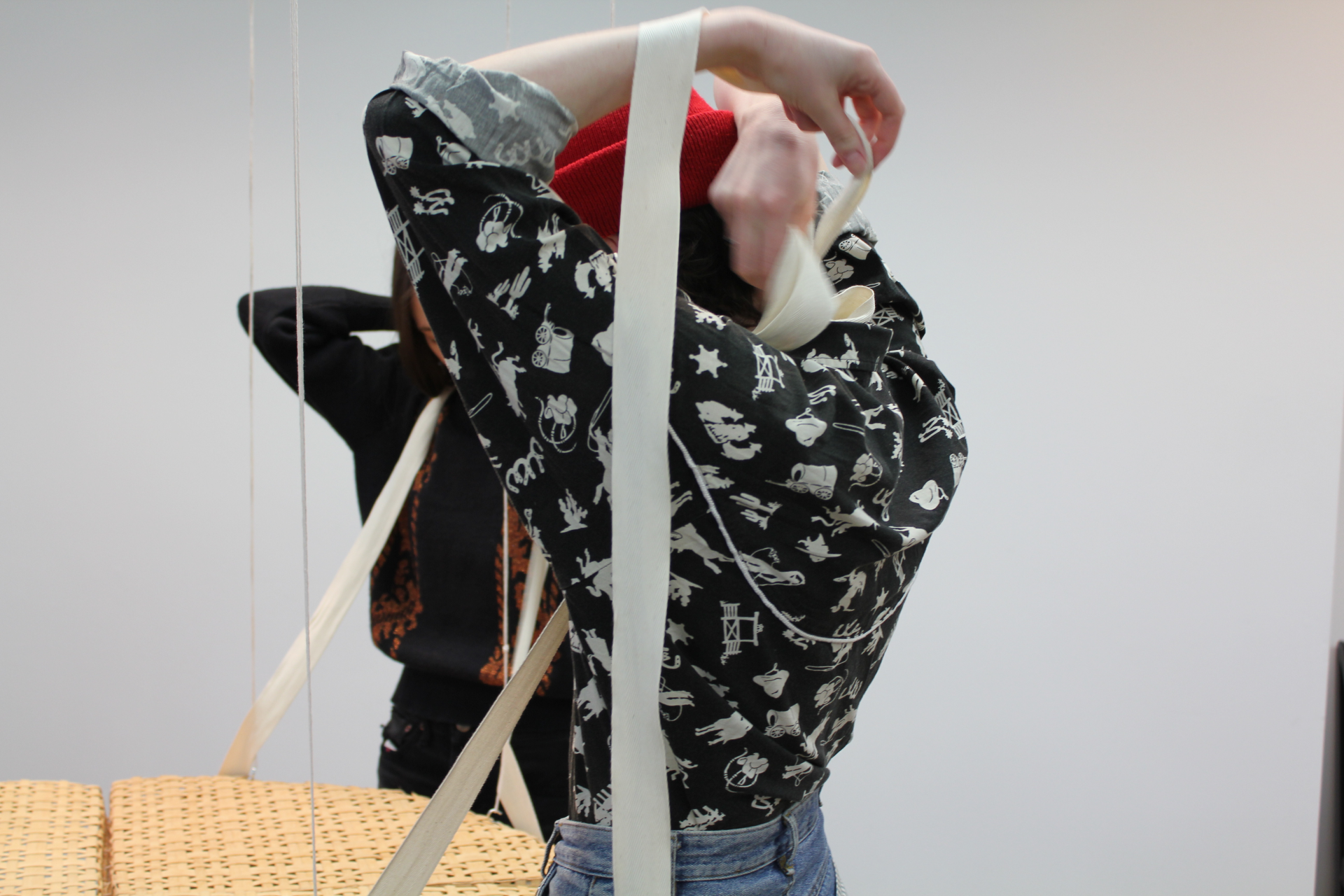 Image capturant l'interactivité de la table avec deux participant.e.s qui attachent des lanières de tissu autour de leur cou pour soutenir la table.
