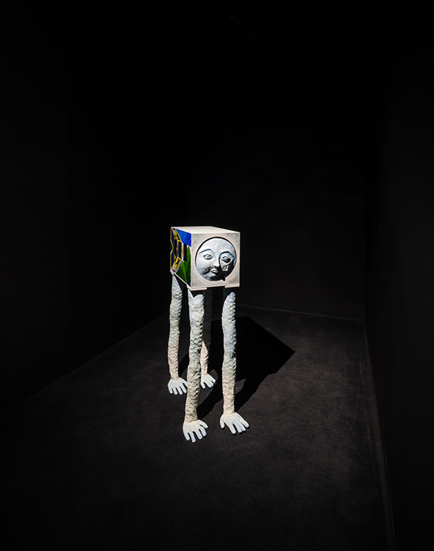 Une sculpture représentant un bus coloré avec de longues jambes blanches et un visage dubitatif dans une chambre noire.