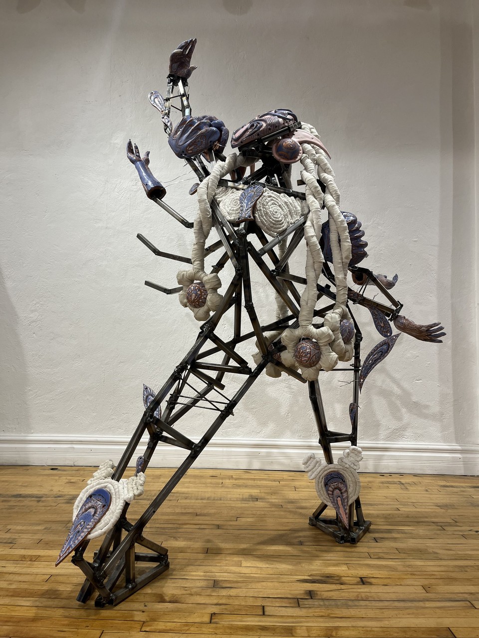 Sculpture représentant une figure robotique composée de pièces métalliques et textiles, l'un de ses quatre bras levé vers le ciel. 