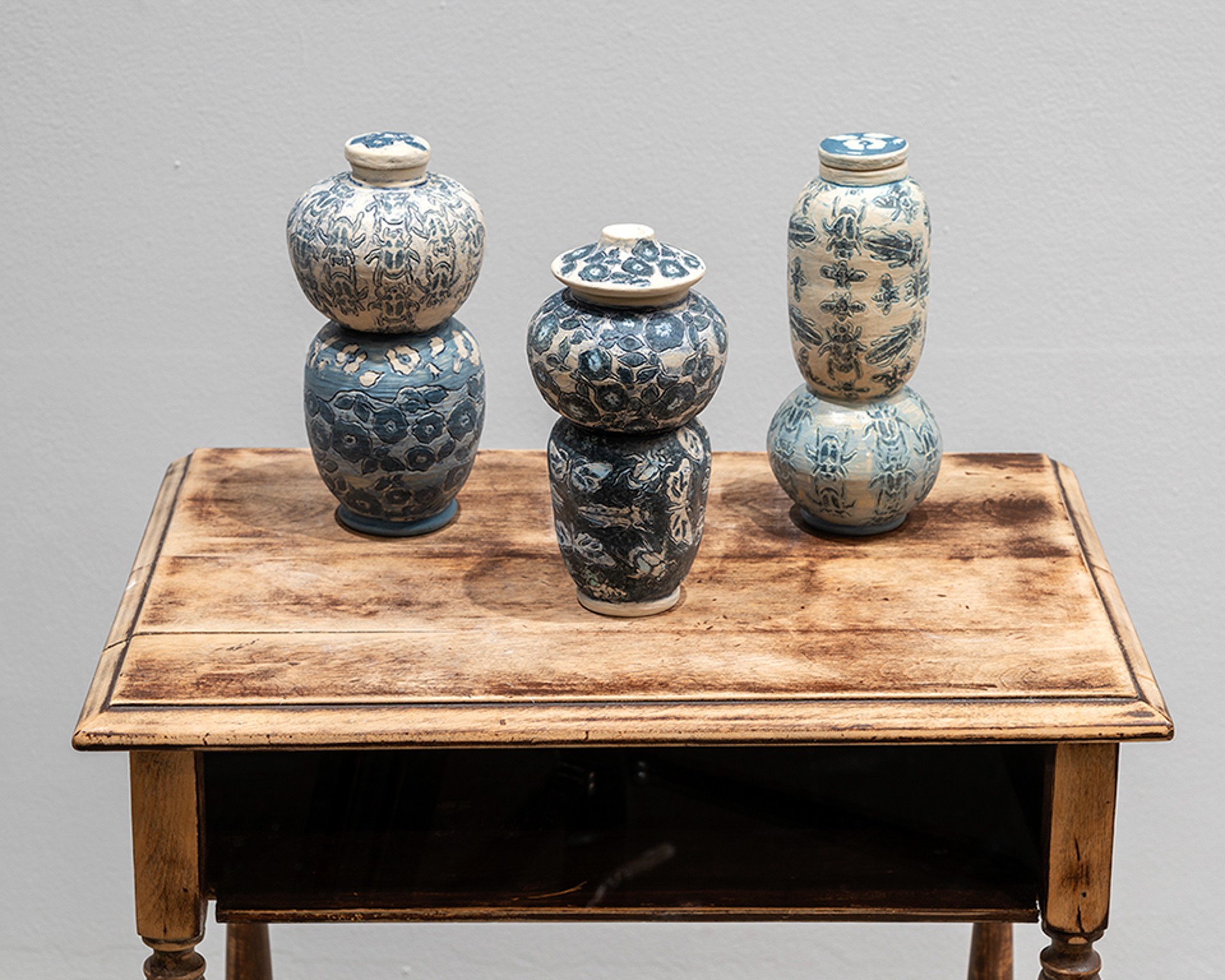 Plusieurs vases en céramique aux couleurs et formes similaires, vus sous différents angles. Les glaçures présentent des touches de pinceau orange, bleu et marron, ainsi qu'un motif estompé de fleurs bleues.
