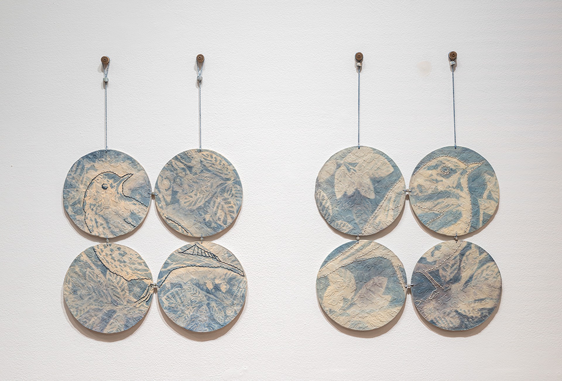 Deux séries de quatre pièces circulaires en céramique sont accrochées au mur. Chaque série de quatre pièces forme l'image d'un oiseau entouré de feuillage.