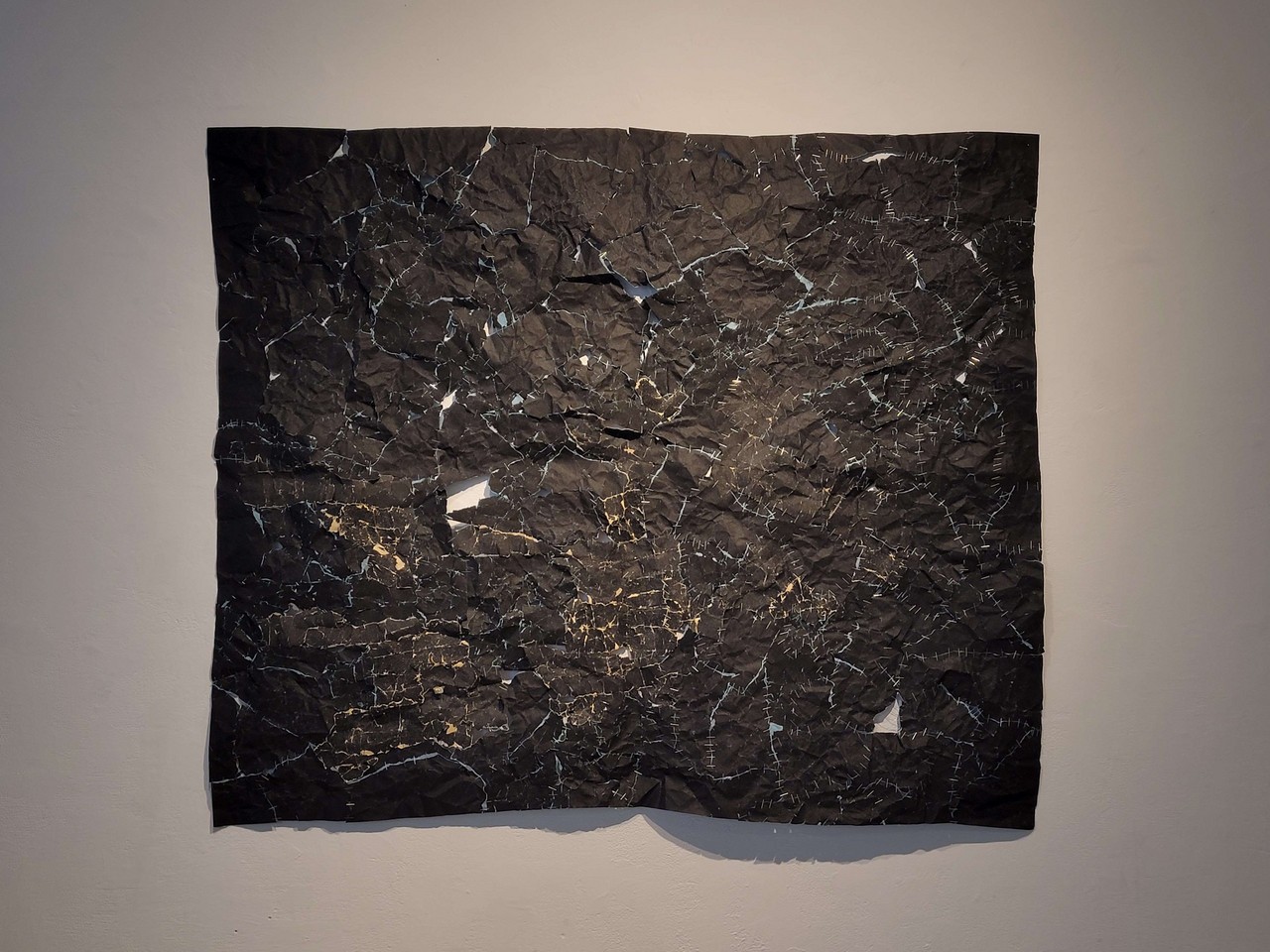 Une pièce rectangulaire composée de nombreux morceaux de papier sablé noir agrafés ensemble.