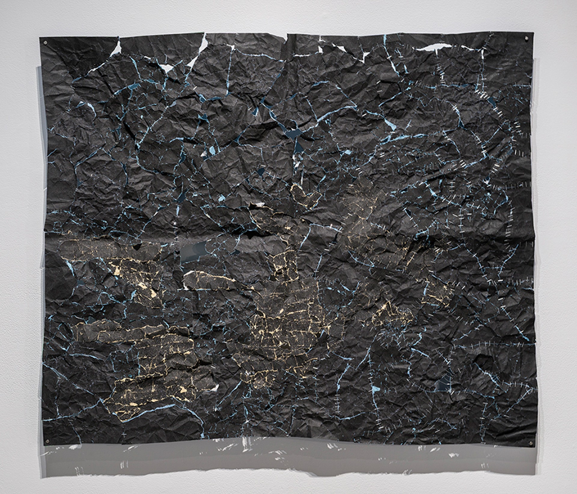 Une pièce rectangulaire composée de nombreux morceaux de papier sablé noir agrafés ensemble.