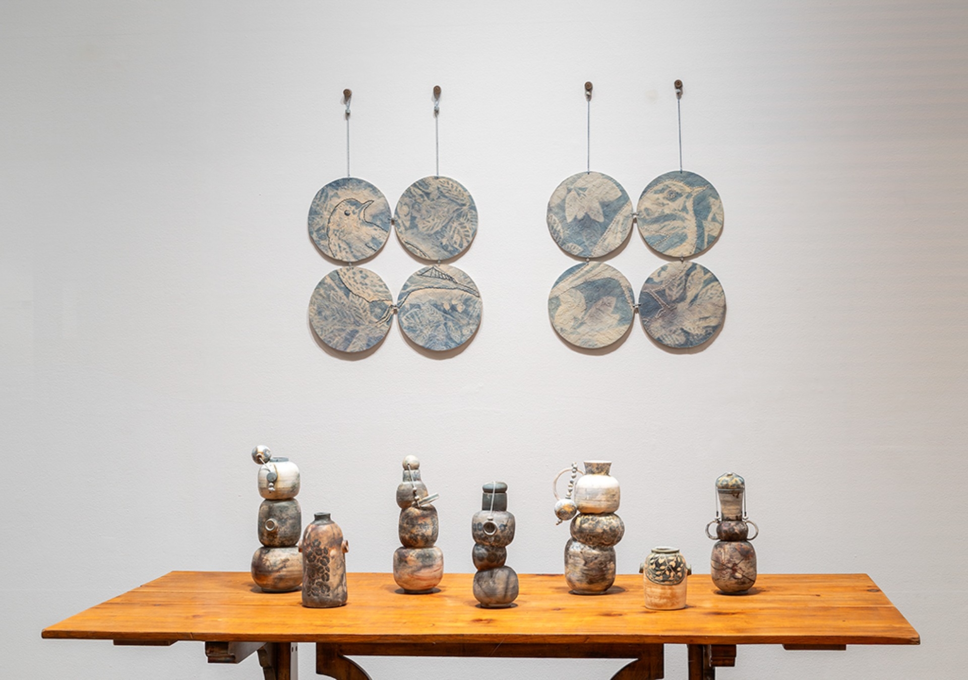 Une installation composée de sept vases en céramique posés sur une table en bois et de deux séries de quatre assiettes rondes bleu pâle accrochées au mur derrière